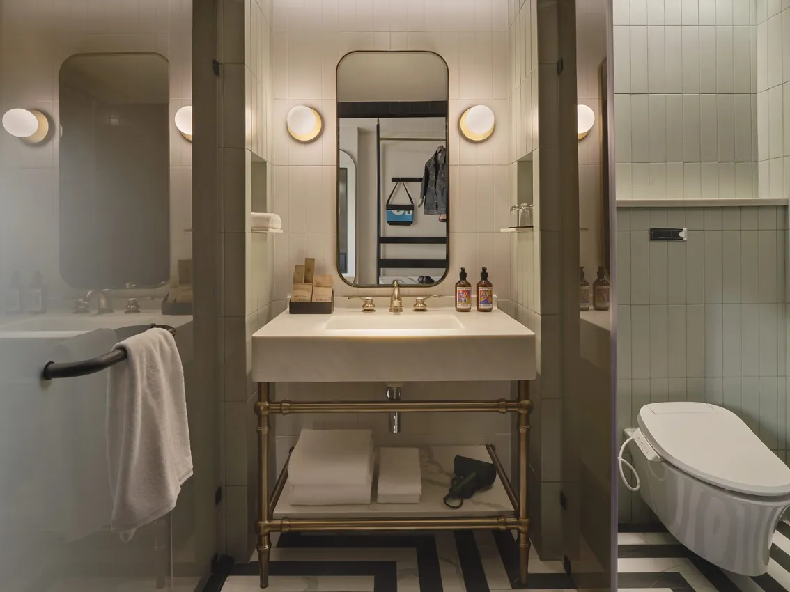 Bathroom vanity with a round mirror, globe lights and a bathtub at Public House Bangkok