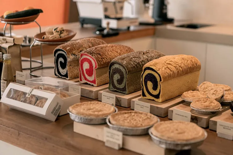 ขนมปัง พาย และเพสตรีวางเรียงบนเคาน์เตอร์ที่ Homework Cafe กรุงเทพฯ