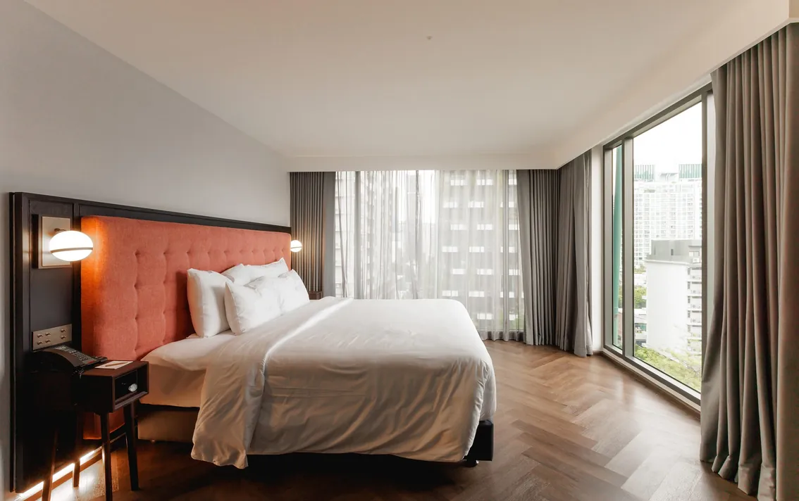 Two-Bedroom Suite bedroom with a coral headboard, herringbone parquet and full-height glazing on two sides