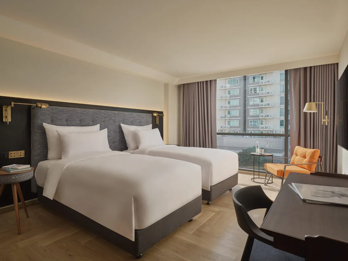 The adjoining Uptown Room of a Two-Bedroom Suite, laid out with twin beds, a city view and an orange armchair