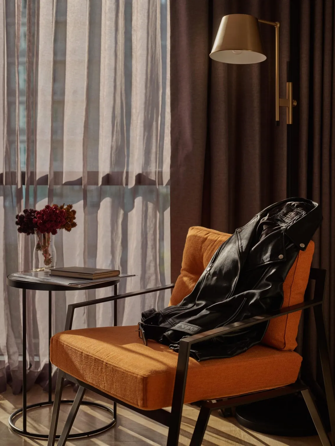 Leather jacket over an orange armchair beside a side table with flowers and a book at Public House Bangkok