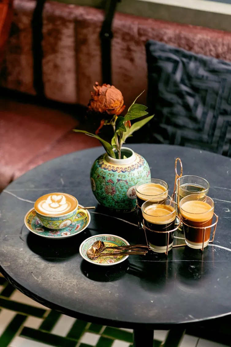 กาแฟ แก้วเอสเพรสโซ และแจกันใบเล็กวางบนโต๊ะหินอ่อนสีเข้มที่ TAMP Kafei and BAR