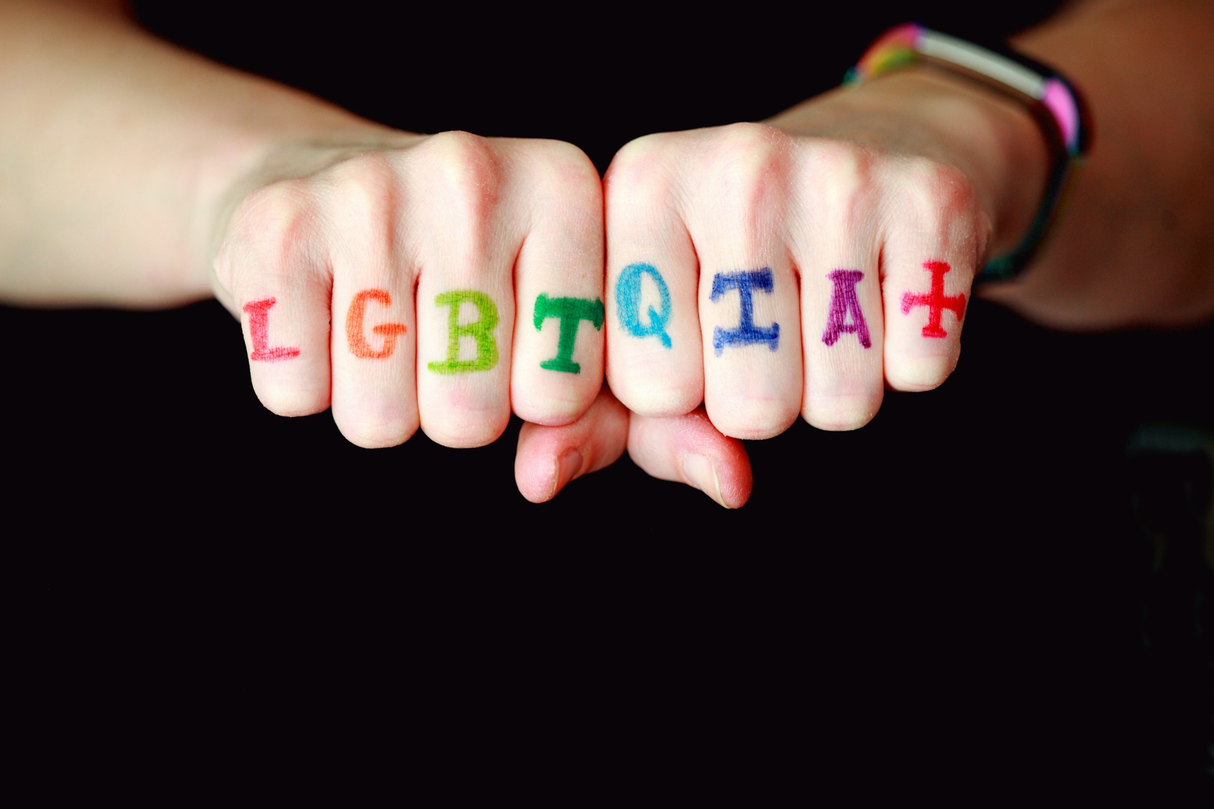 A hand with LGBTQIA+ painted across the knuckles in rainbow letters