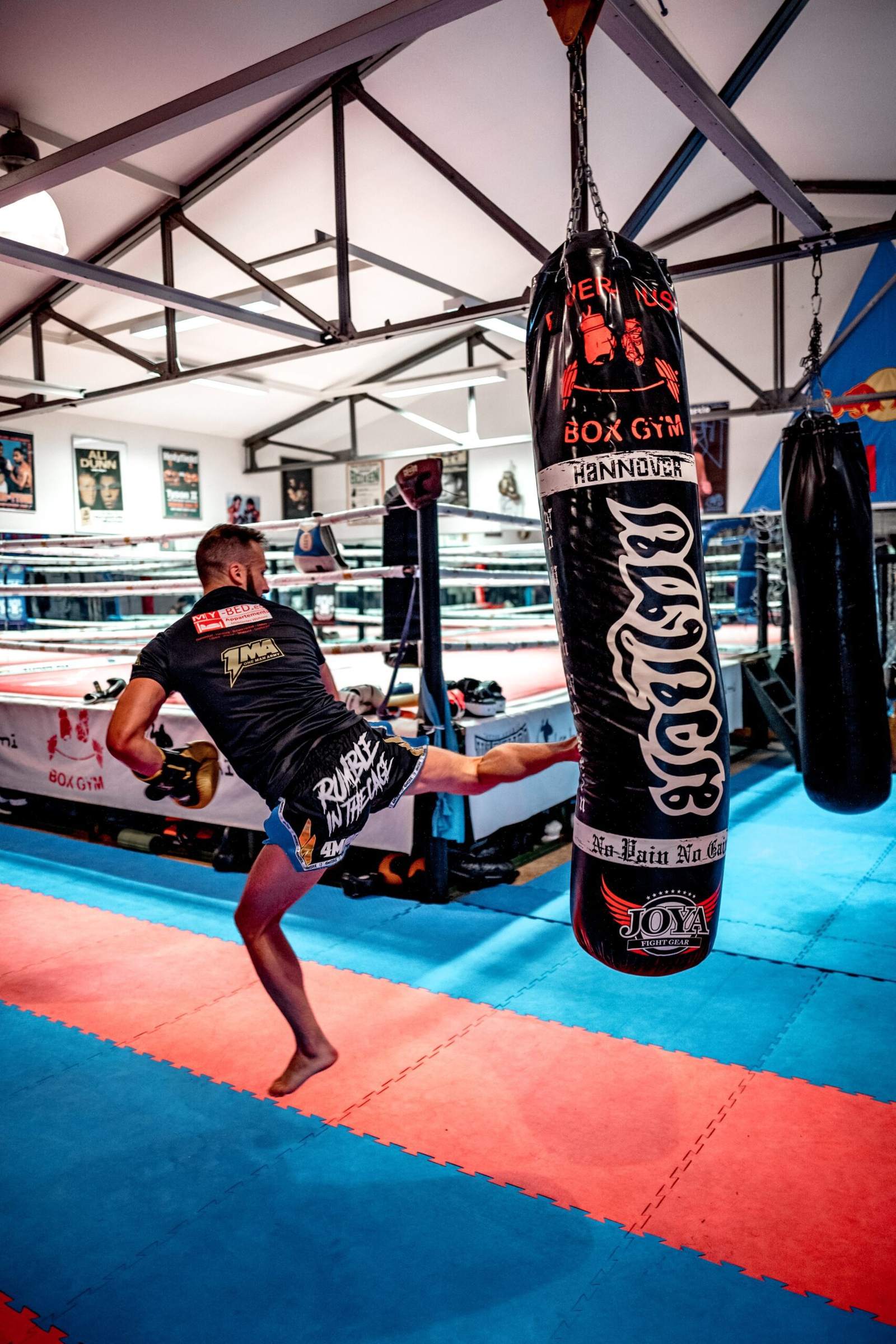 A boxer training on a heavy bag beside a Muay Thai ring