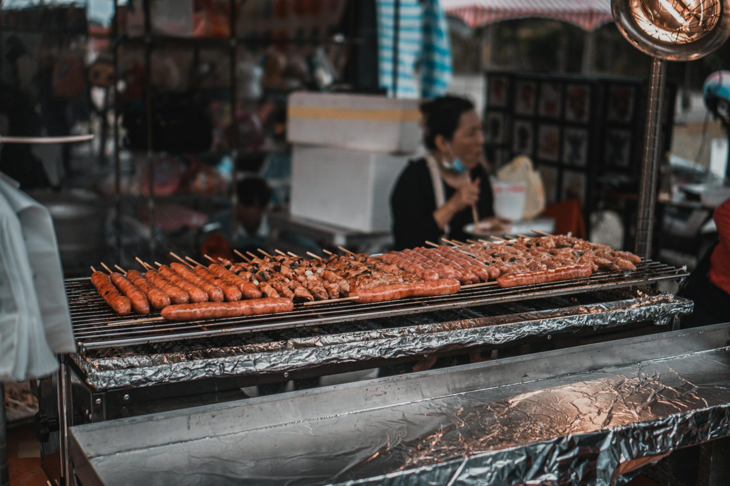 Pork skewers grilling over charcoal at a Bangkok street stall