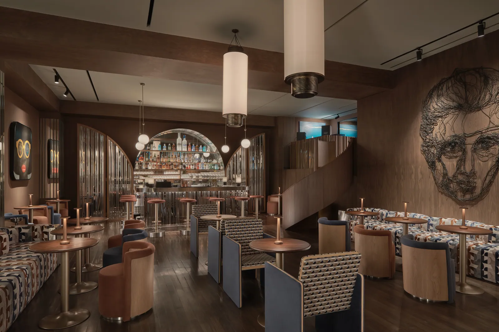 The dining room at SWD on the Lobby Floor of Public House Bangkok, round tables and banquettes under pendant lights, with the arched bar at the far end