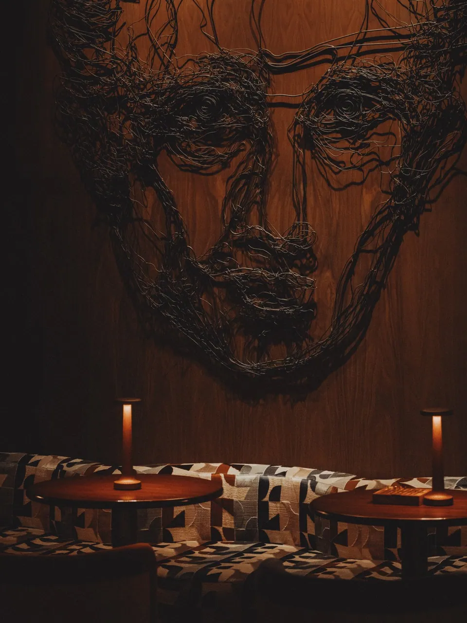 A wire-drawn portrait on the wall above the candle-lit bar counter at Public House Bangkok