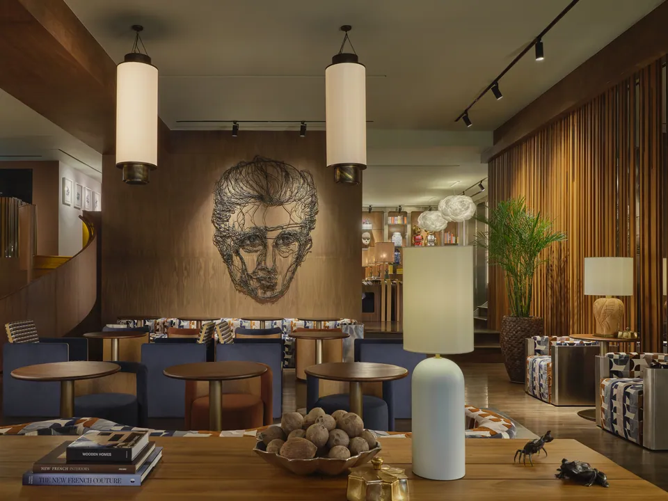 A drawn portrait mural above the navy banquettes in FORUM at Public House Bangkok, with cylinder pendant lights over a timber table of books and objects