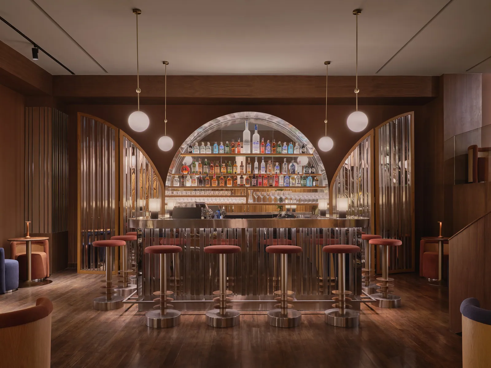 The lit back bar at Public House Bangkok, with globe pendants over a run of stools beneath an arched bottle display