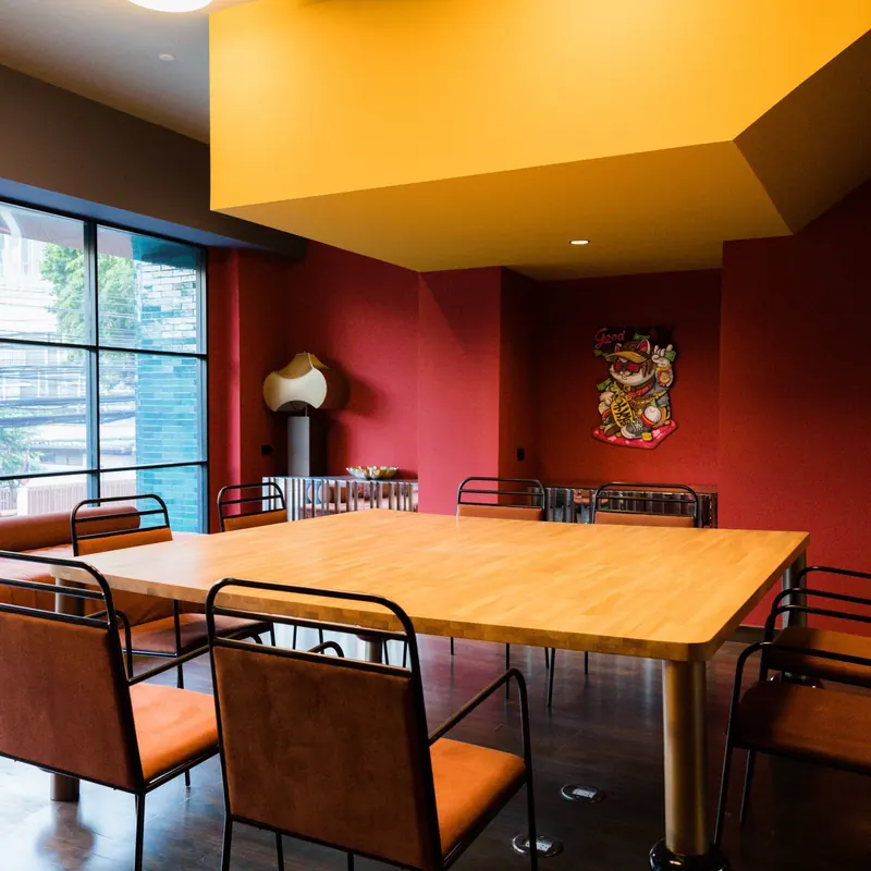 The FLEXI-ROOM at Public House Bangkok laid out around one long timber table, under a mustard soffit between red walls and a full-height window
