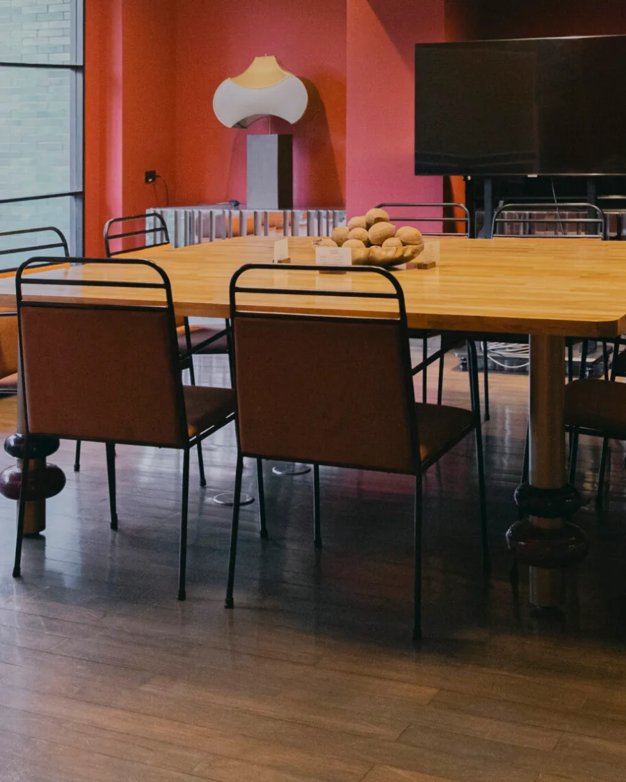 The FLEXI-ROOM at Public House Bangkok seen across the timber table, with black-framed chairs and a screen on the red wall under a shell-shaped light