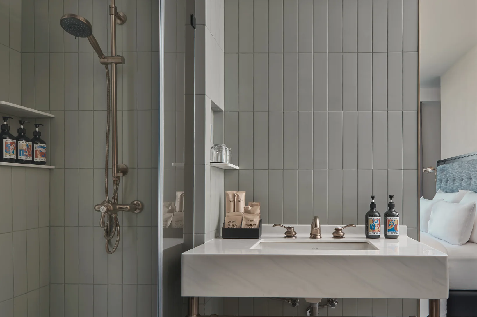 A rain shower and marble washstand in a guest bathroom at Public House Bangkok, amenities on the tiled shelf