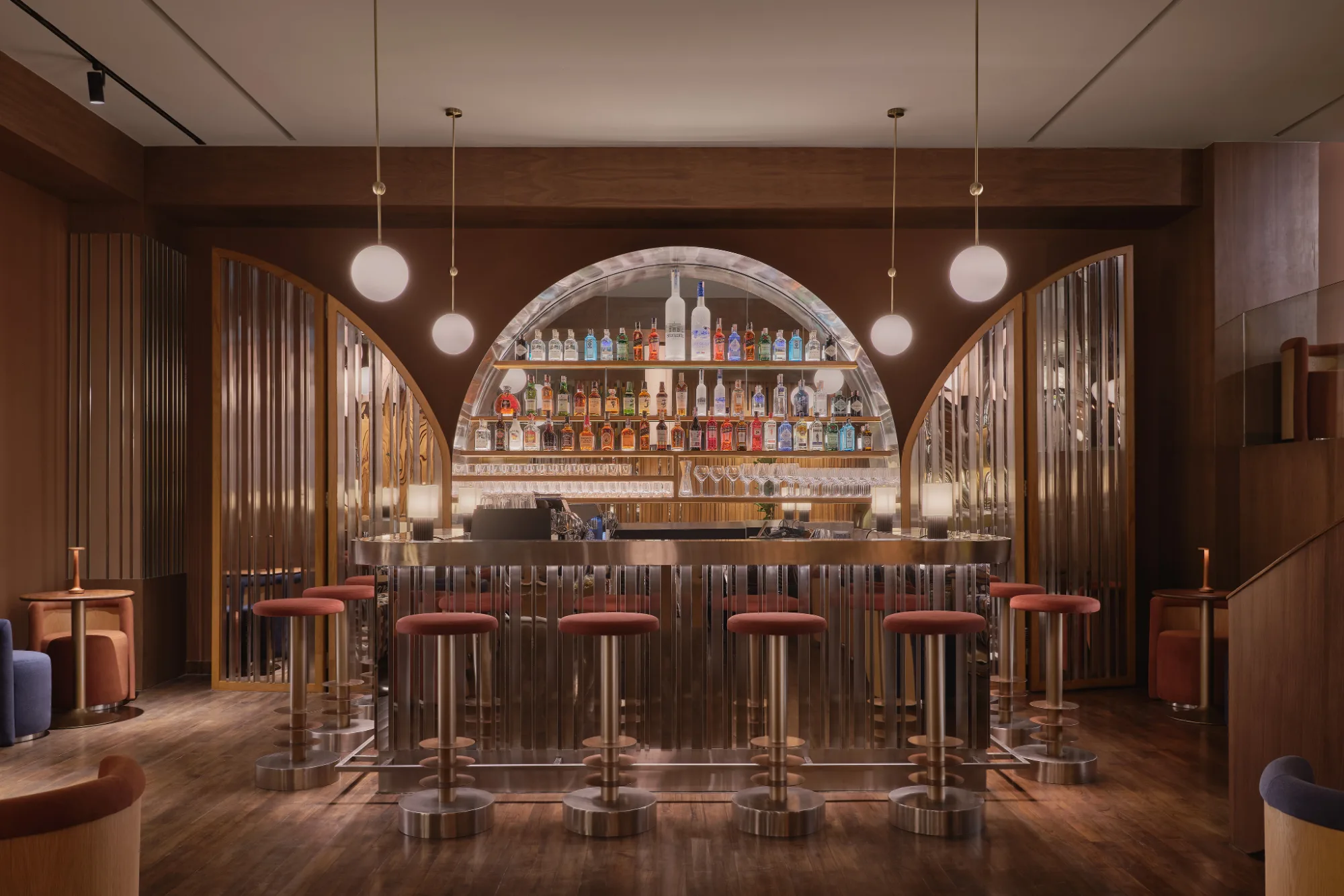 The arched, lit back bar at OPEN BAR, Public House Bangkok, stools along the counter under glass pendants