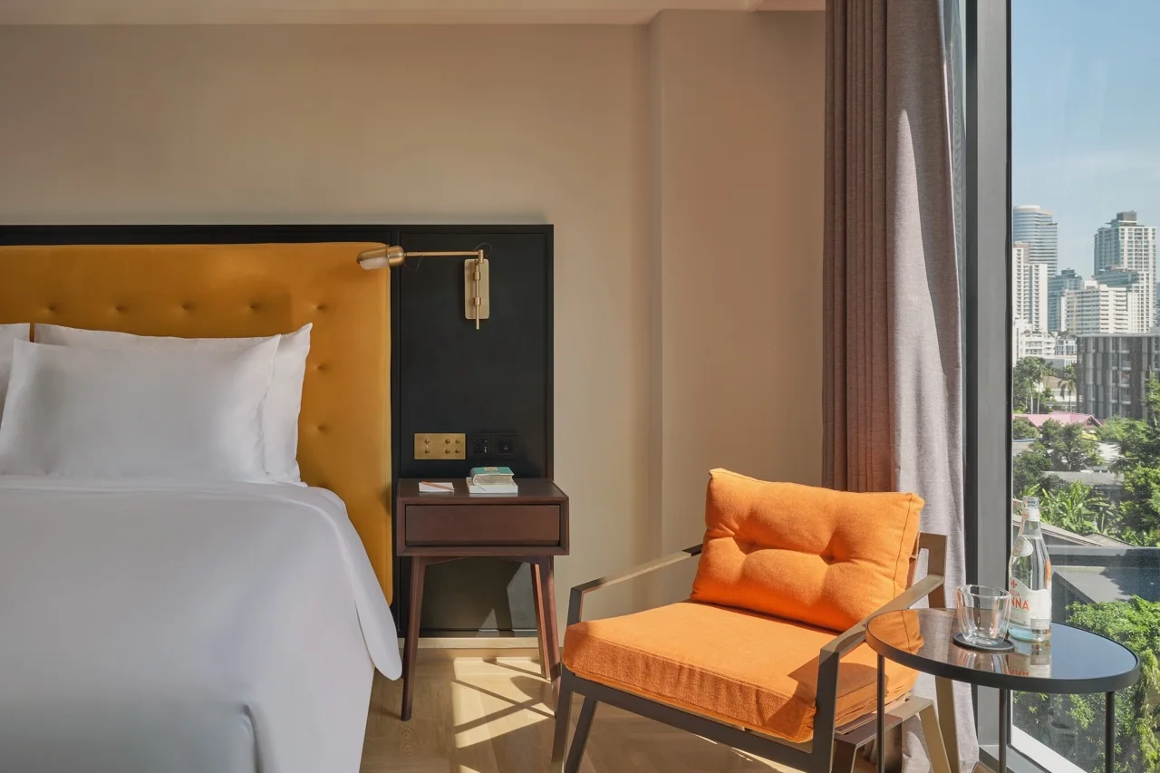 A corner guest room at Public House Bangkok, an orange armchair beside the floor-to-ceiling window