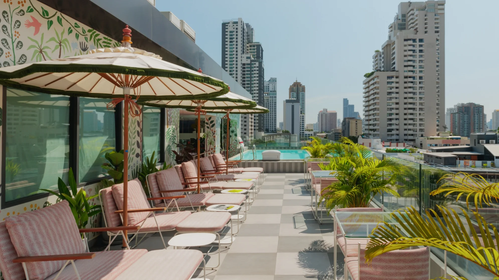 Paper parasols over striped sun loungers on the rooftop at Public House Bangkok, the swimming pool and the Sukhumvit skyline beyond
