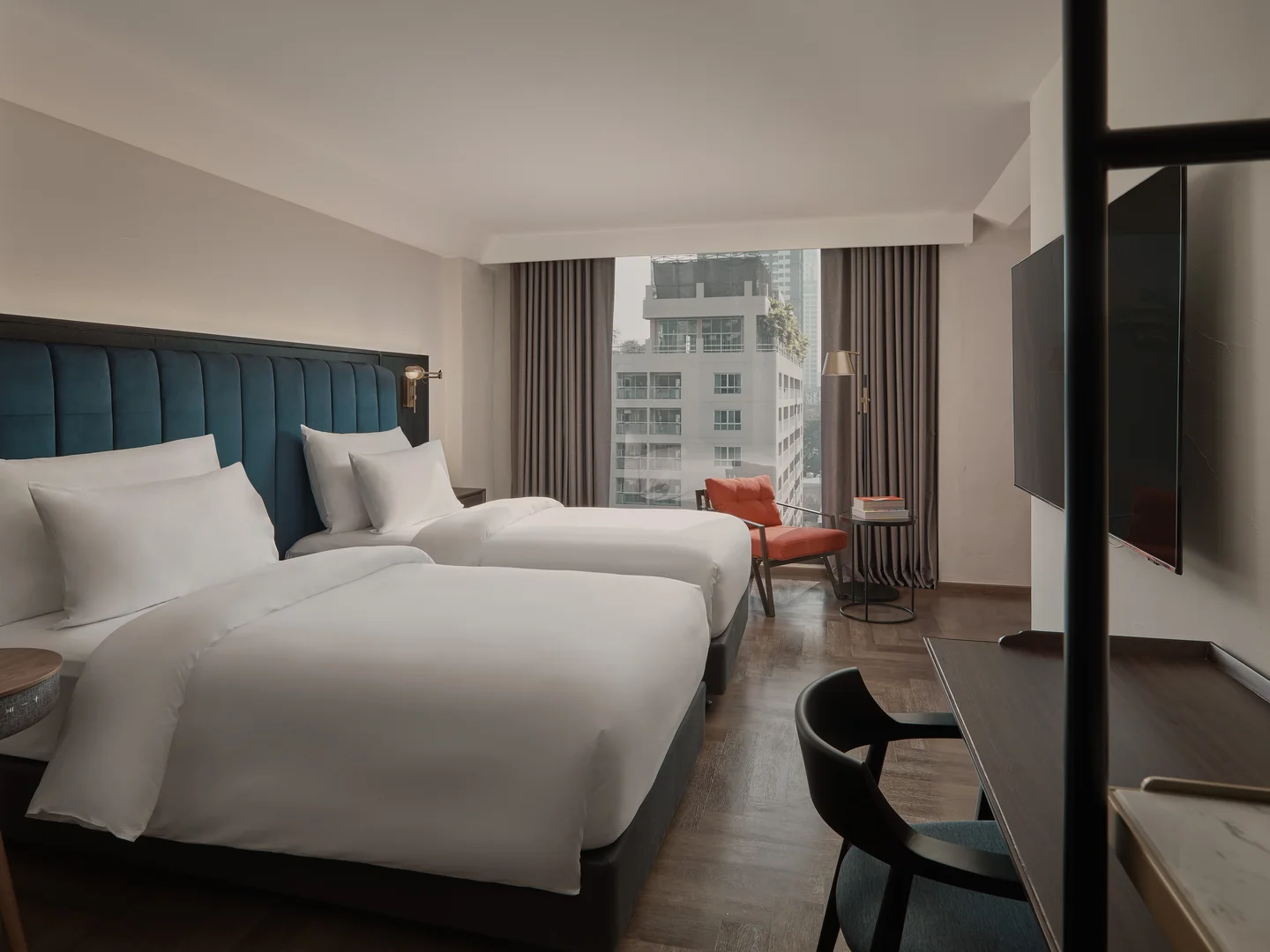Twin beds and a red sofa beneath a city window in the 34 sqm Day Dreamer Room at Public House Bangkok