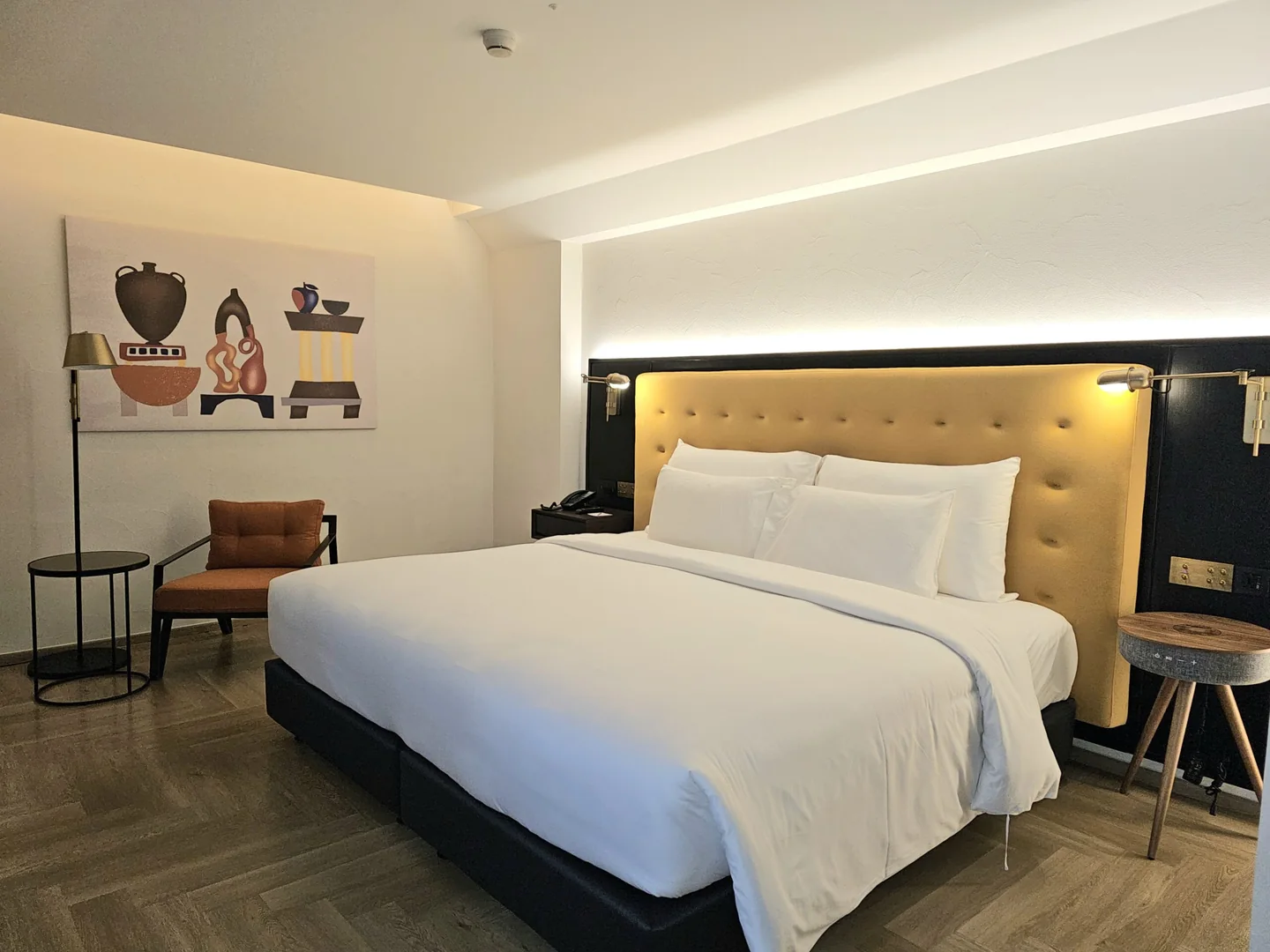 A king bed with a mustard tufted headboard in the 28 sqm Downtown Room at Public House Bangkok