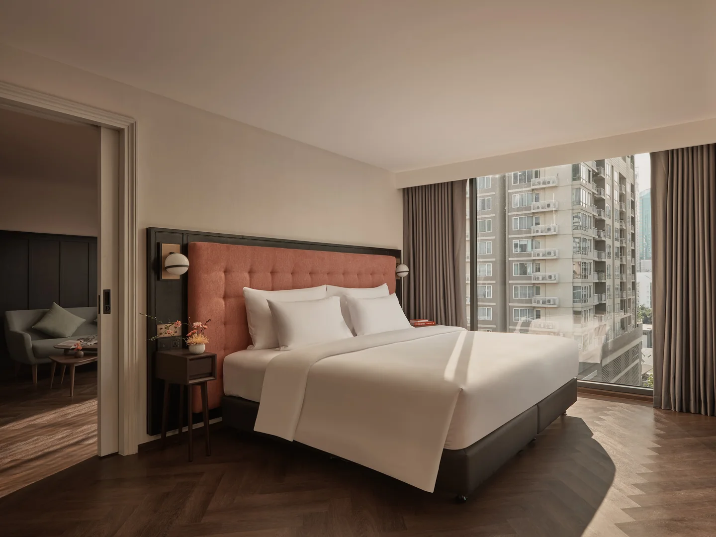 The bed of the 55 sqm Junior Suite at Public House Bangkok, with a terracotta headboard and the separate living area through the door